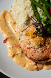 Pan-seared salmon steak with crispy breadcrumb topping, creamy roasted red pepper sauce, mashed potatoes, sautéed green beans and microgreens on a restaurant-style plate