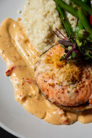 Pan-seared salmon steak with crispy breadcrumb topping, creamy roasted red pepper sauce, mashed potatoes, sautéed green beans and microgreens on a restaurant-style plate