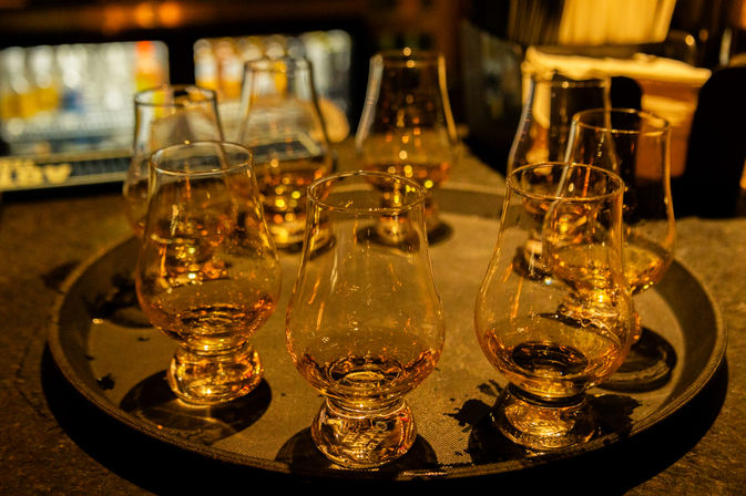 Amber whiskey samples in tulip-shaped tasting glasses arranged on a round tray at a dimly lit bar with warm golden reflections.