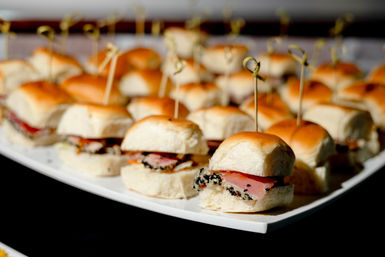 Party-ready platter of mini smoked salmon sliders on soft dinner rolls with sesame-crusted filling and cocktail picks, elegant event appetizer