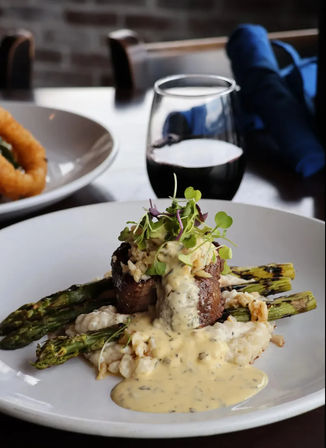Gourmet filet mignon medallion on risotto and grilled asparagus, drizzled with creamy herb sauce and microgreens, with a glass of red wine on a restaurant table