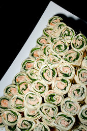 Stacked spinach and smoked salmon cream-cheese pinwheel wraps on a white catering platter — bite-sized party appetizer and finger food.