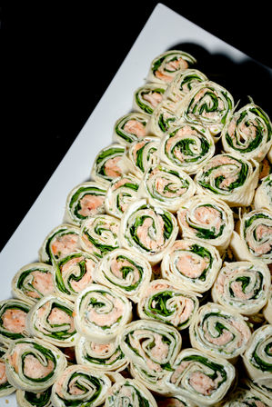 Stacked spinach and smoked salmon cream-cheese pinwheel wraps on a white catering platter — bite-sized party appetizer and finger food.