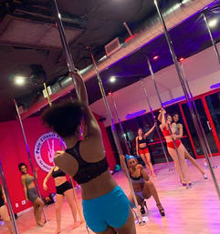 Energetic group pole fitness class with women in athletic wear practicing pole dance moves on chrome poles in a vibrant, brightly lit studio
