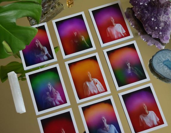 Twelve polaroid-style aura photography prints arranged in a grid on a gold mirror, surrounded by amethyst, blue agate slice, selenite wand and a green leaf.