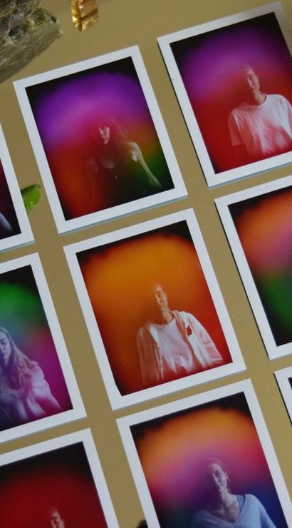 Twelve polaroid-style aura photography prints arranged in a grid on a gold mirror, surrounded by amethyst, blue agate slice, selenite wand and a green leaf.