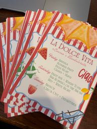 Stack of beach-themed 'La Dolce Vita' bachelorette itinerary cards with red-and-white stripes, umbrella, pizza slice and cocktail illustrations