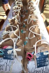 Sunlit rows of burlap beach-style gift bags with sunglasses, teal votive holders and ribbon tags on a rustic wooden table — coastal party favors in Carmel