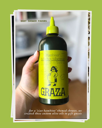 Hand holding a bright green-labeled olive oil bottle styled as a 'ciao bambino' baby shower favor, with a playful pregnant-woman illustration and bold label — a fun kitchen gift or party favor.