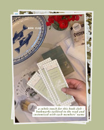 Cozy book club tabletop: hand holding three pale green personalized bookmarks, blue-and-white fish plate, red flower centerpiece, packet of oyster crackers and wrapped napkins on a cream tablecloth.