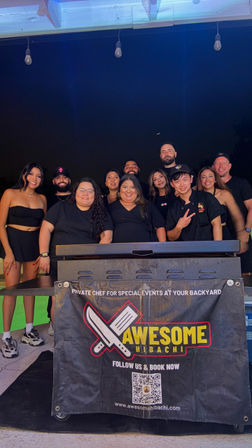 Smiling group of friends and a hibachi chef posing behind a griddle at an outdoor backyard party at night, string lights overhead and a branded event banner on the grill