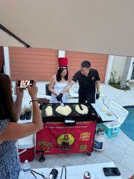 Poolside backyard hibachi in Florida: chef guides a guest at a griddle shaping fried rice into "I ♥ U" while another person snaps a photo.