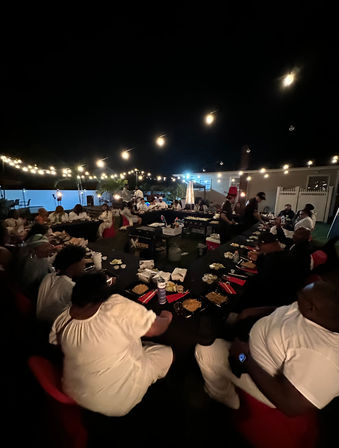 Cozy backyard outdoor dinner party at night with long communal tables under string lights, guests enjoying plated meals and drinks in a festive patio setting