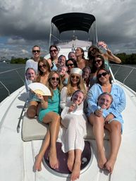 Yacht party: group of women on a boat in a coastal bay under dramatic clouds, posing and smiling while holding playful cutout face props
