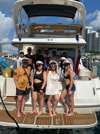 Group of friends wearing captain hats on a yacht at a sunny coastal marina with high-rise skyline