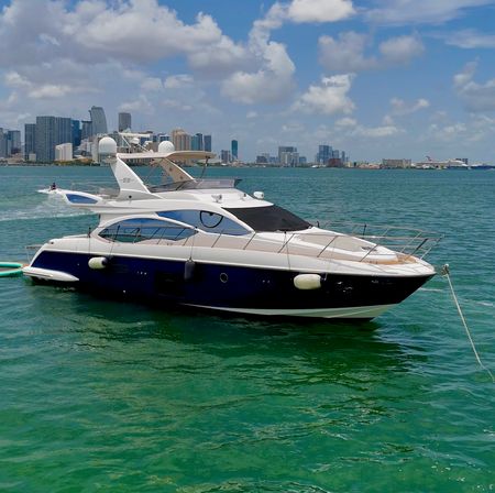 Luxury white-and-blue motor yacht anchored in turquoise Miami Bay with downtown skyline and partly cloudy sky