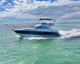 Sleek motor yacht slicing sunlit turquoise water under a dramatic partly cloudy sky, leaving a foamy white wake