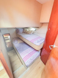 Cozy yacht cabin with two compact stacked bunk beds in lavender sheets and striped throws, small round porthole, beige walls and glossy wood-paneled door.
