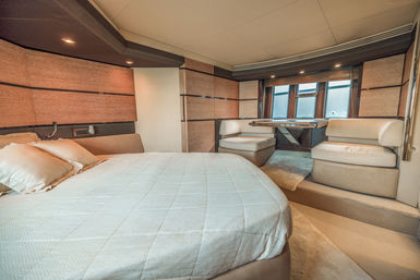 Luxury yacht stateroom with cozy queen bed, built-in banquette dining nook, wood-accent walls and large windows in a modern neutral-toned interior.