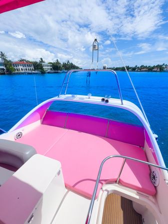 Vibrant pink boat sunpad and seating overlooking turquoise water, palm-lined waterfront homes and a sunny blue sky.