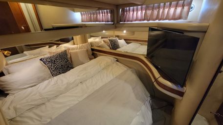 Cozy yacht stateroom with white bedding, navy coral-pattern throw pillow, mirrored walls, porthole curtains and a wall-mounted flat-screen TV