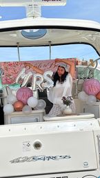 Bride-to-be posing on a white yacht at a marina with silver "MRS" balloon, pink "Future Mrs" balloons, floral "Bride to Be" banner and bouquet for a fun bridal shower celebration.