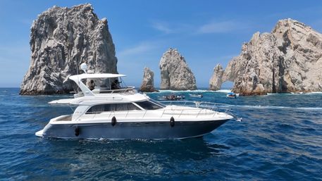 White luxury yacht cruising deep blue ocean under a clear sky in front of the iconic granite rock formations and natural arch (El Arco) at Land's End, Cabo San Lucas, Mexico.