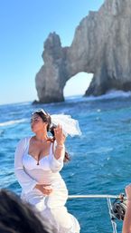 Bride in a white dress and veil playfully posing on a boat near El Arco (Lands End) rock formation in Cabo San Lucas with turquoise sea and clear blue sky
