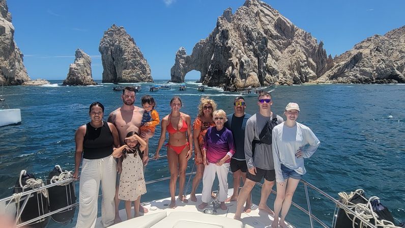 Multigenerational group posing on a boat in front of the iconic El Arco rock formation at Land's End, Cabo San Lucas, with bright blue sea and sunny sky.