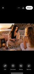 Sunset beach tarot reading — a reader shuffles tarot cards on a blanket with crystals and candles while a client listens on the sand near rocky coastal cliffs