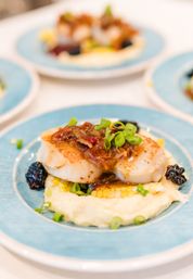 Seared scallops with caramelized onion relish and sliced scallions atop creamy mashed potatoes and corn, accented with blackberries on a blue plate — restaurant-style seafood entree.