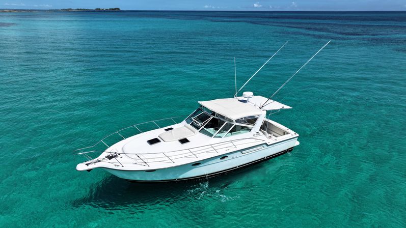 White sportfishing yacht floating on crystal-clear turquoise tropical sea with distant low islands and a bright blue sky