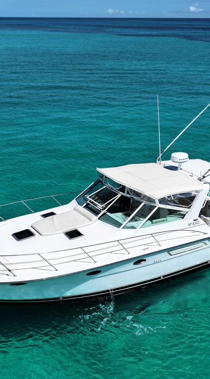 White sportfishing yacht floating on crystal-clear turquoise tropical sea with distant low islands and a bright blue sky