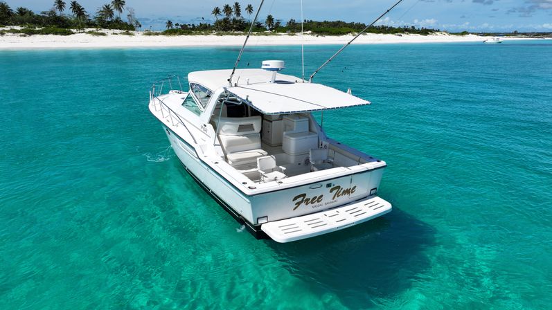Sleek white motorboat floating in crystal-clear turquoise Bahamas waters off a white sandy beach lined with palm trees under a bright blue sky
