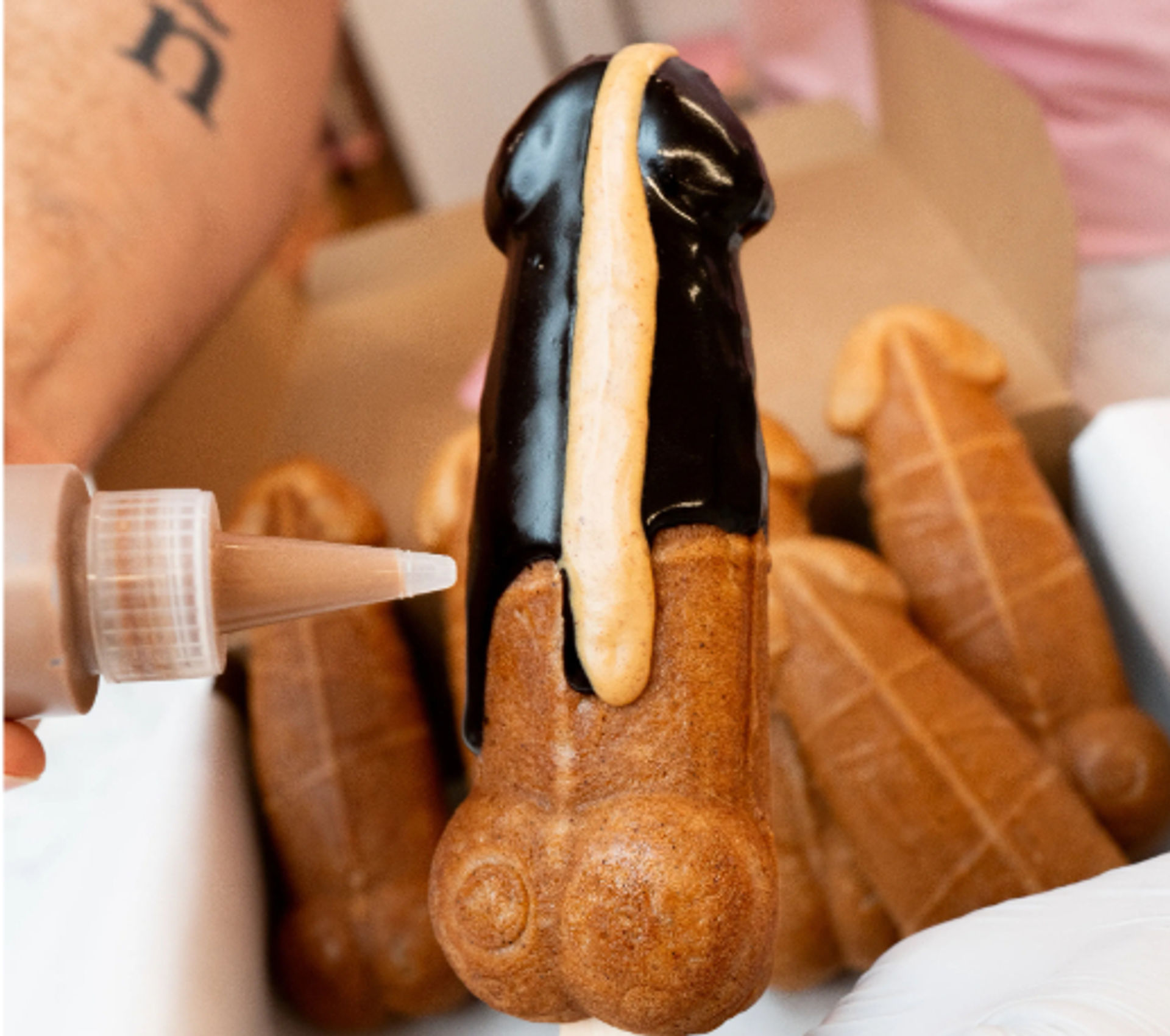 Novelty phallic-shaped eclair dipped in dark chocolate with a stripe of cream being piped, boxed dessert