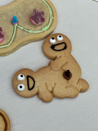 Close-up of playful gingerbread cookies with smiling icing faces and a candy button, stacked on a white tablecloth — festive holiday cookie shot