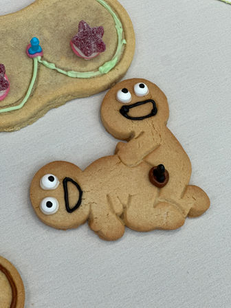 Playful gingerbread cookies: two-person gingerbread with candy eyes, black-icing smiles and a candy button on a white tablecloth, beside a star-gumdrop decorated cookie
