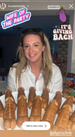 Smiling woman in a home kitchen at a bachelorette-style party, standing behind a tray of novelty bread rolls with stickers that read “Wife of the Party” and “It’s Giving Bach.”