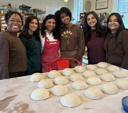 Smiling group of women makers in a pottery studio standing behind a table of textured, handmade clay bowl forms drying.