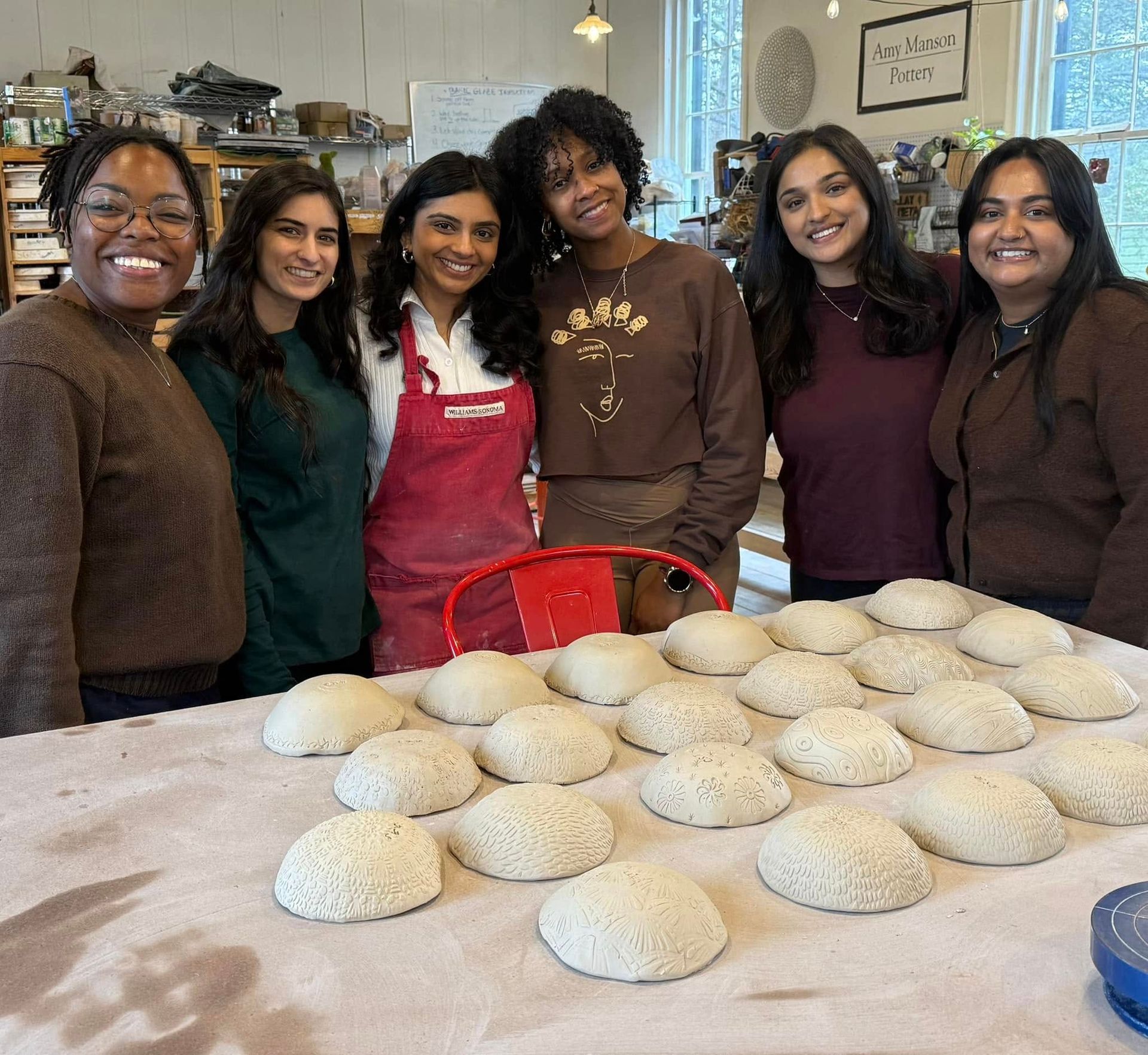 Smiling group of women makers in a pottery studio standing behind a table of textured, handmade clay bowl forms drying.