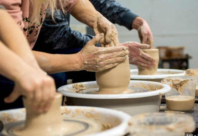 Close-up of hands shaping wet clay on spinning pottery wheels during a group ceramics workshop