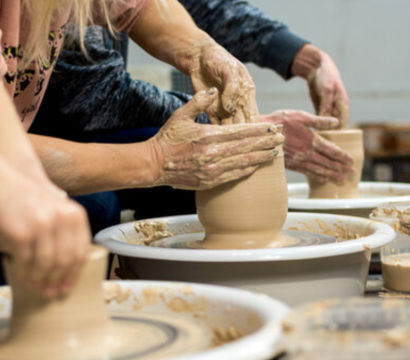 Close-up of hands shaping wet clay on spinning pottery wheels during a group ceramics workshop
