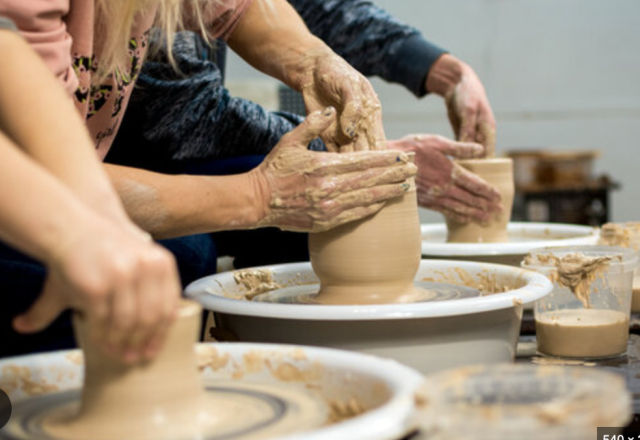 Close-up of hands shaping wet clay on spinning pottery wheels during a group ceramics workshop