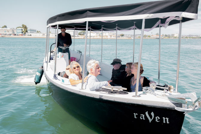 Small covered sightseeing boat with a group of adults and a captain enjoying a relaxing harbor cruise on turquoise coastal waters under a sunny sky