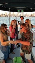 Group of friends sipping champagne and toasting on a covered party boat with a downtown skyline and harbor at sunset.