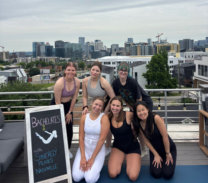 Six women smiling on a rooftop yoga/pilates mat after a bachelorette workout with the Nashville skyline in the background.