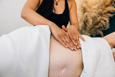 Maternity massage — therapist’s hands gently massaging a pregnant belly under white towels in a soothing spa setting