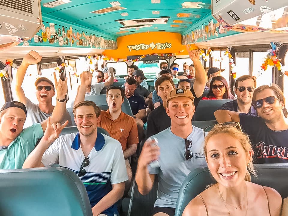 Smiling group of young adults cheering inside a colorful, decorated Texas party bus