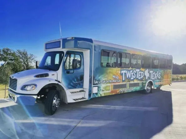 Colorful Texas-themed party shuttle bus with vibrant wrap parked on a sunlit concrete lot under a clear blue sky