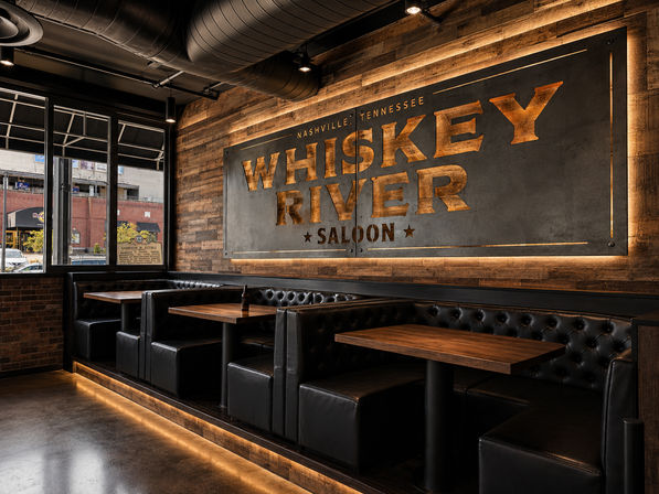 Rustic Nashville saloon interior with tufted black leather booths, wooden tables and walls, a large backlit metal sign, warm under-seat and pendant lighting, and a street view through front windows